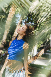 Junge Frau mit geschlossenen Augen genießt den Schatten der Palmenblätter - PBTF00216
