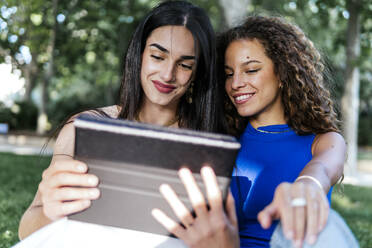 Lächelnde Freundinnen benutzen gemeinsam einen Tablet-PC im Park - PBTF00225