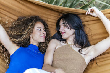 Smiling lesbian couple looking at each other and lying in hammock - PBTF00228