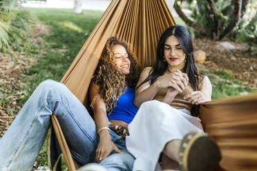 Smiling girlfriends spending leisure time in hammock - PBTF00230