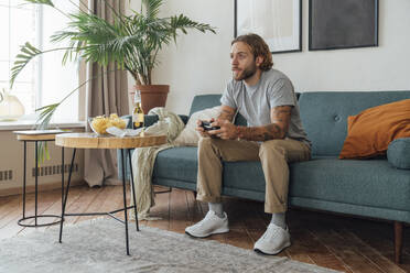 Young man playing video game with controller at home - VPIF08466