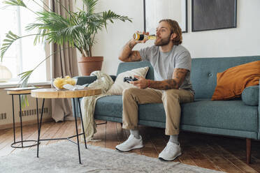 Young man drinking beer and playing video game at home - VPIF08467