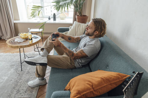 Young man playing video game with controller in living room - VPIF08475