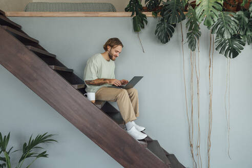 Smiling businessman working on laptop at home - VPIF08491