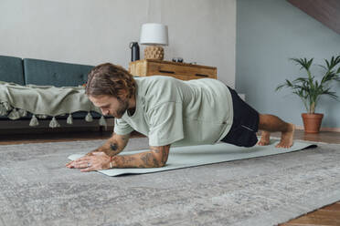 Junger Mann übt Yoga auf einer Matte zu Hause - VPIF08501