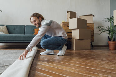 Smiling young man folding carpet at home - VPIF08507