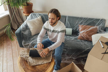 Junger Mann packt Vase und sitzt zu Hause auf dem Sofa - VPIF08529