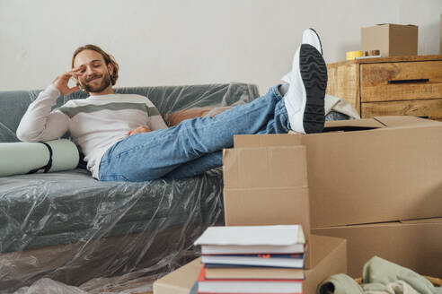 Smiling man sitting on sofa in living room at home - VPIF08532