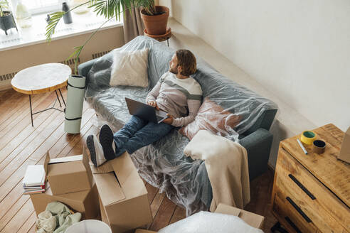 Young freelancer sitting with laptop on sofa at home - VPIF08536