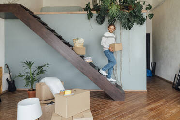Young man moving down with cardboard box on staircase - VPIF08540