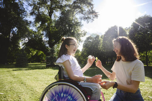 Happy daughter in wheelchair with mother enjoying at park - EYAF02732