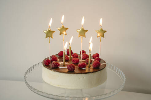 Tempting cake with burning candles on table in front of wall - YBF00150