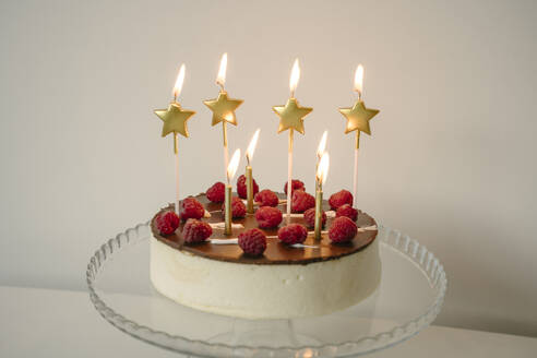 Verlockende Torte mit brennenden Kerzen auf einem Tisch vor einer Wand - YBF00150