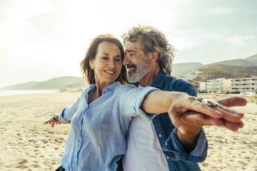 Glücklicher Mann und Frau stehen mit ausgestreckten Armen an einem sonnigen Tag am Strand - OIPF03472