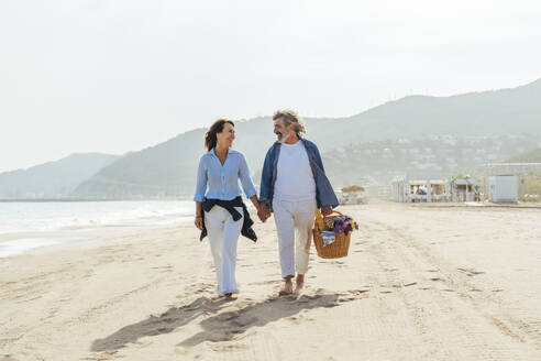 Glücklicher Mann hält Korb und geht mit Frau am Strand spazieren - OIPF03473