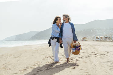 Glückliche Frau umarmt Mann und geht mit Korb am Strand an einem sonnigen Tag - OIPF03479