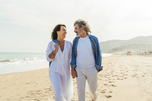 Glücklicher älterer Mann und Frau spazieren am Strand an einem sonnigen Tag unter Himmel - OIPF03487