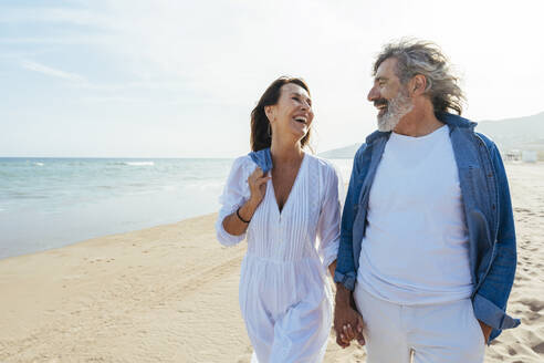 Glückliche ältere Frau hält die Hände mit einem Mann und geht am Strand spazieren - OIPF03489