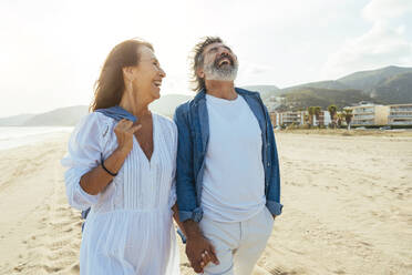 Cheerful couple holding hands and walking at beach - OIPF03491