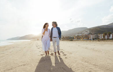 Glückliches Paar hält sich an den Händen und spaziert am Strand unter dem Himmel an einem sonnigen Tag - OIPF03492