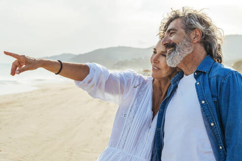 Smiling senior woman gesturing with man standing at beach - OIPF03493