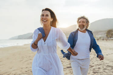 Glückliche Frau hält Händchen mit Mann, der am Strand spazieren geht - OIPF03497