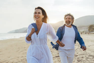 Happy woman holding hands with man walking at beach - OIPF03497