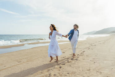 Happy senior woman holding hands with man and walking on shore - OIPF03498
