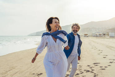 Happy woman holding hands with man and running on shore - OIPF03499