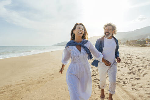 Happy senior couple holding hands and running at beach - OIPF03501