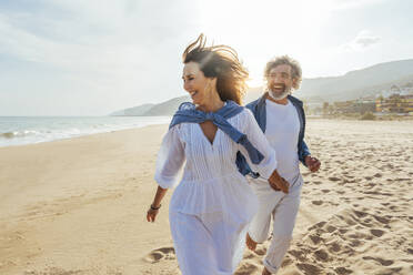 Cheerful senior couple holding hands and running at beach - OIPF03502