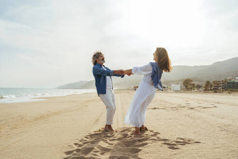 Happy senior couple holding hands and standing together at beach - OIPF03504