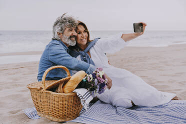 Happy senior woman taking selfie through smart phone with man at beach - OIPF03511