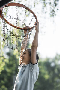 Lächelnder Junge hängt am Basketballkorb - ANAF02054