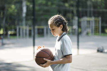 Junge hält Basketball auf einem Sportplatz - ANAF02055