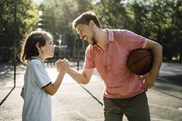 Glücklicher Vater mit Basketball, der die Hand seines Sohnes im Gericht hält - ANAF02062