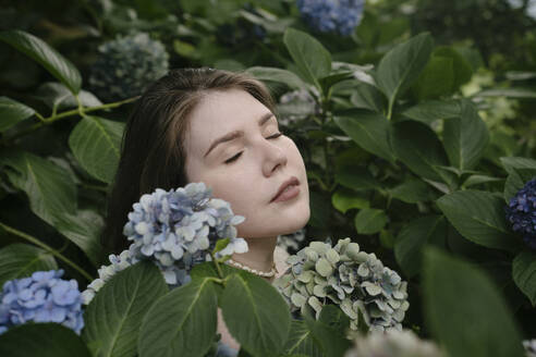 Gelassene Frau mit geschlossenen Augen inmitten von Hortensienblüten - YBF00153
