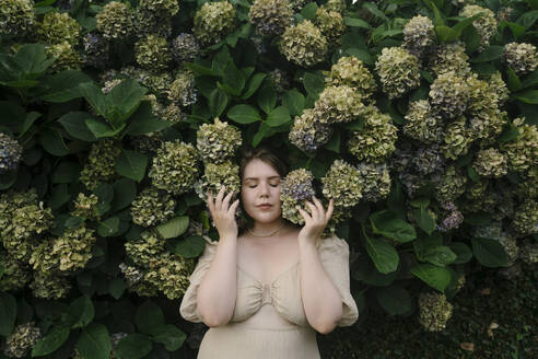 Schöne Frau steht vor Hortensienpflanzen im Garten - YBF00159