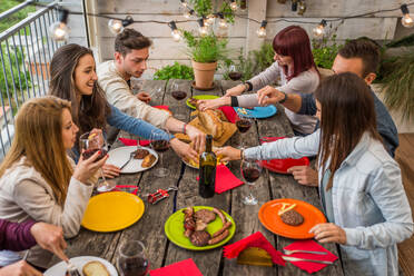 Group of happy friends bonding at home - Young adults having lunch and spending time together on a rooftop balcony, cooking meat on barbecue - DMDF03680