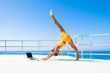 Beautiful young atlethic woman wearing sportswear doing yoga meditation on the terrace rooftop with sea view and blue sky - Yoga practicer training outdoors, healthy lifestyle, sport and meditation concept - DMDF03713