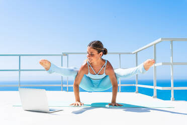 Beautiful young atlethic woman wearing sportswear doing yoga meditation on the terrace rooftop with sea view and blue sky - Yoga practicer training outdoors, healthy lifestyle, sport and meditation concept - DMDF03758