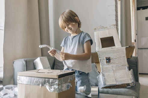 Smiling blond boy making astronaut suit at home - EVKF00003