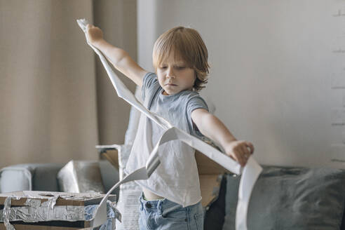 Boy with foil paper making astronaut suit in living room - EVKF00006