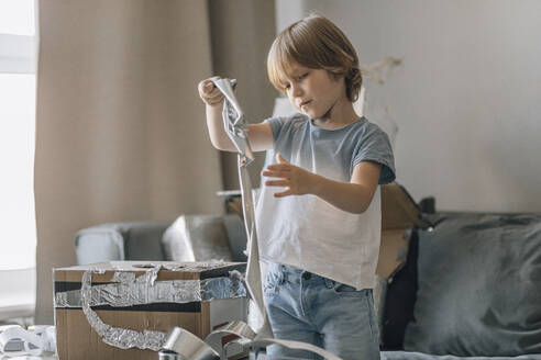 Boy with silver foil paper making astronaut suit at home - EVKF00007