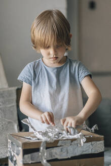 Blond boy making astronaut robot suit at home - EVKF00008