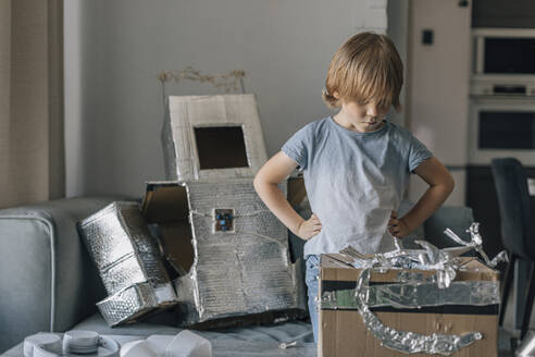 Boy with hands on hips looking at astronaut suit in living room - EVKF00010