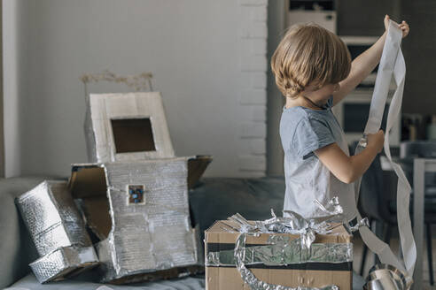 Blond boy with foil paper making astronaut suit at home - EVKF00011