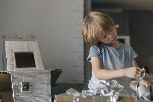 Focused boy with silver foil paper making astronaut costume - EVKF00012