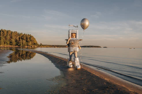 Boy in astronaut costume holding silver balloon at beach - EVKF00022