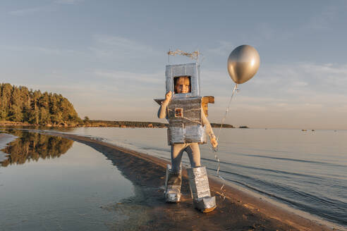 Junge im Astronautenanzug hält silbernen Luftballon am Strand - EVKF00023